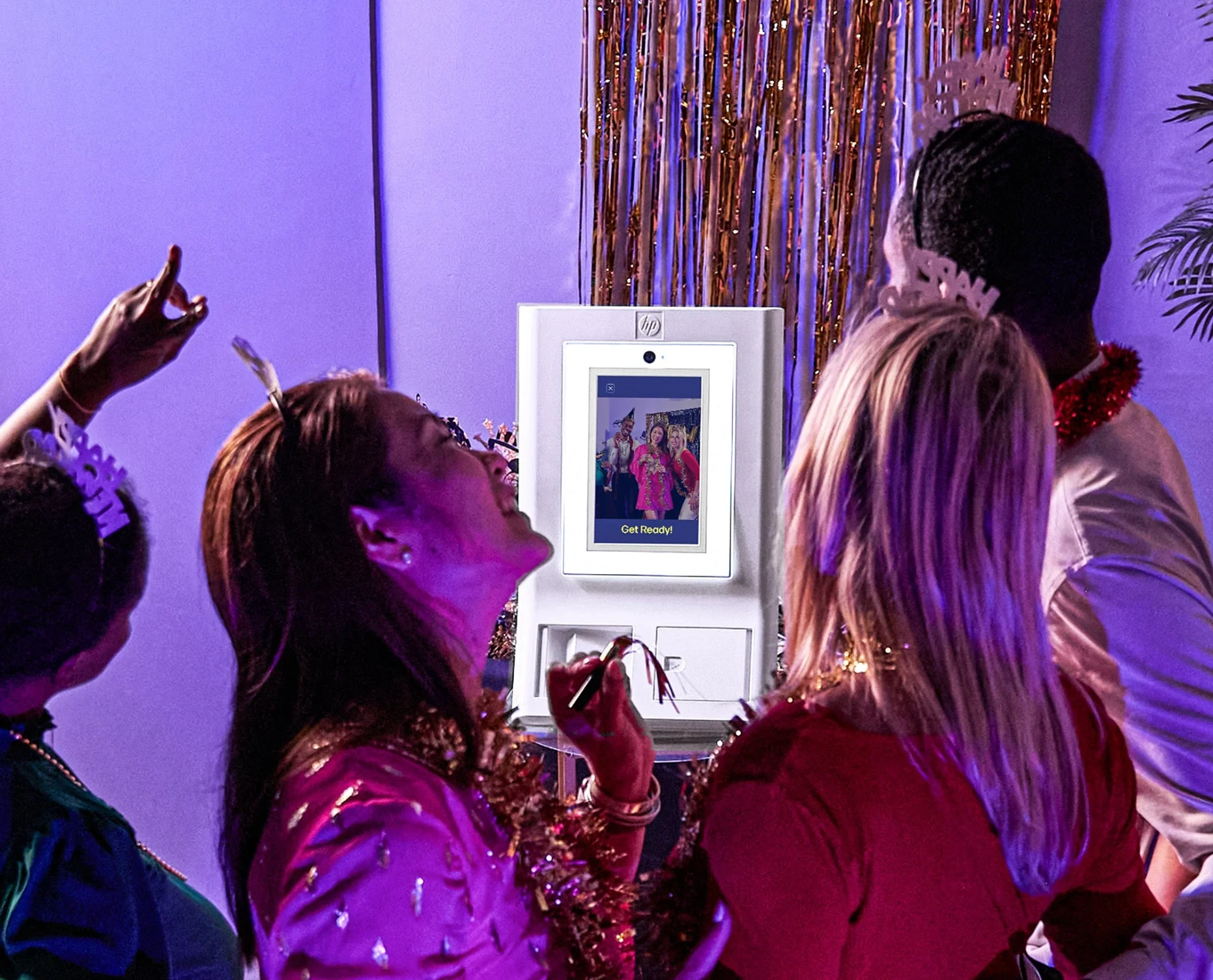 Guests posing together at a white photo booth with a touchscreen, surrounded by colourful party lighting